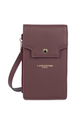 Sac bandoulière en cuir violet Lancaster Paris avec rabat et fermeture par bouton-pression, design fin et bracelet de poignet sur fond blanc.