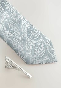 Gaiši zilas paisley stila kaklasiksna ar strukturētu audumu, kas apvienota ar spīdīgu sudraba kaklasiksnas spiesti, kas izceļas ar elegantu dizainu un klipša mehānismu.