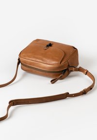Tan leather crossbody bag with a zippered compartment and a flap. Features an adjustable strap and a smooth texture. Compact rectangular shape.