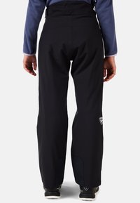 Svarta snöbyxor med hög midja, elastiskt band och slick design. Har förstärkta lappar vid vristerna och en logotyp på baksidan.