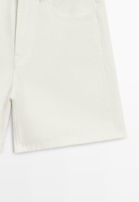 Shorts en denim blanc montrant la poche avant, l'ourlet et le détail de la fente latérale sur un fond clair uni.