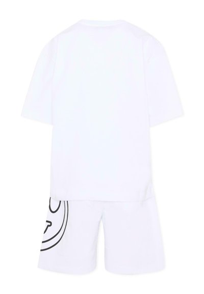 Chemise blanche à manches courtes assortie à un short blanc avec un grand motif circulaire noir sur la cuisse gauche.