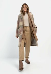 Wollmischung Karo-Mantel in gedämpften Pastellfarben, mit großen Taschen, einem Reverskragen und einem lockeren Schnitt, kombiniert mit beigen Hosen und braunen Stiefeln.