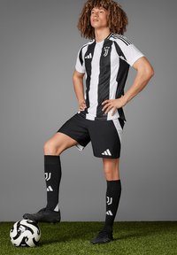Juventus fodboldtrøje med sort-hvide lodrette striber, sorte shorts og sorte sokker med et logo, paired med sorte støvler og en bold.