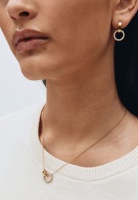 Orecchini a cerchio dorati con piccoli strass trasparenti, abbinati a una delicata collana in oro con pendente circolare.