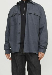 Grå skjorta med knappar i texturerat tyg, två bröstfickor, rak skärning och långa ärmar, tillsammans med mörk denimjeans.