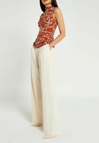 Hnědočervený bezrukávový top s bílým abstraktním vzorem, spárovaný s krémovými širokými kalhotami a nahými špičatými podpatky.