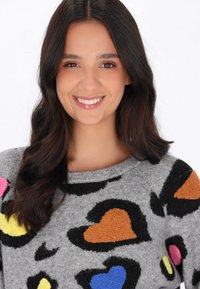 Maglione grigio con scollo a girocollo, caratterizzato da motivi a cuori e macchie testurizzati in rosa, giallo, blu, nero e marrone. Tessuto morbido.