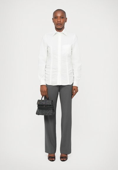 Camicia bianca con finitura testurizzata, pantaloni grigi a gamba dritta, borsa nera con design strutturato e sandali neri con cinturini.