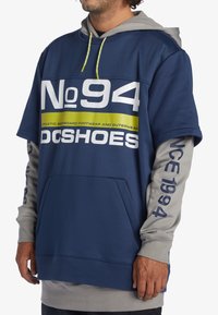 Blå och grå tröja med luva med stort "No 94" och "DC SHOES"-text; har en känguruficka och dragsko i huvan. Accentuerade ärmar.
