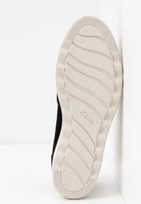 Semelle d'une chaussure noire avec semelle en caoutchouc beige présentant des motifs de bande de roulement ondulés et le logo Clarks au centre.