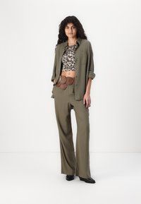 Camisa verde-oliva e calças largas verde-oliva combinadas com um top cropped de padrão de leopardo e um cinto circular castanho com recortes. Sapatos pretos.