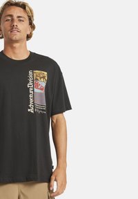 Musta puuvillainen t-paita, jossa on monivärinen graafinen kuvasto edessä, mukaan lukien teksti ja abstraktit kuviot, lyhyillä hihoilla ja rentolla istuvuudella.