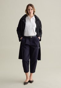Chaqueta exterior negra, camisa blanca de botones, pantalones azul marino y bailarinas negras. La chaqueta tiene una capucha y bolsillos; los pantalones son cortos con un ajuste relajado.