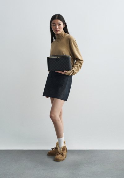 Μαύρη τσάντα με επένδυση και φερμουάρ, φορεμένη με χρυσό μπλουζάκι μακρυμάνικο και σκούρα τζιν φούστα. Καφέ μπότες με γουνάκι και λευκές κάλτσες.