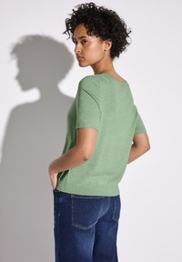 Pull léger vert clair à manches courtes en tricot doux, avec un col rond et une coupe décontractée, associé à un jean ample bleu marine.