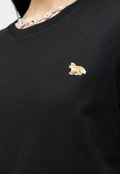 Μαύρο πουκάμισο με μια μικρή κεντημένη πορτοκαλί αλεπού στο αριστερό στήθος και μια ασημένια περιδέραιο με πολύτιμη πέτρα γύρω από τον λαιμό.