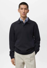 Sudadera de color azul marino con cuello, dos botones y un ajuste relajado. Llevada sobre una camisa de cuello azul claro, mostrando una textura suave.