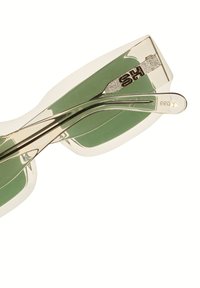 Sluneční brýle s průhledným světle béžovým rámem, zelenými skly a stříbrnými akcenty. Mají zakřivený design a texturované stranice.