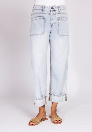 Light blue wide-leg jeans with rolled cuffs worn with tan open-toe flat sandals on a plain background.