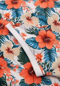 Blommigt tyg med stora orange och gräddfärgade blommor med gröna blad på en vit bakgrund; mjuk textur med en slät finish.