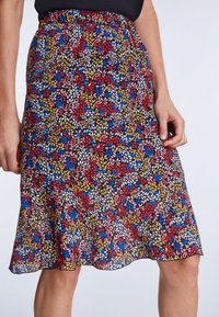 Jupe florale avec un motif de feuilles colorées en rouge, bleu, jaune et blanc sur un fond noir ; taille élastique ; ourlet s'évase doucement.
