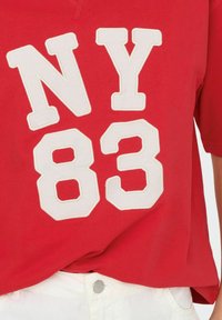 Rode t-shirt met korte mouwen met grote witte cijfers "NY 83" op de voorkant, gemaakt van zacht katoen jersey materiaal.