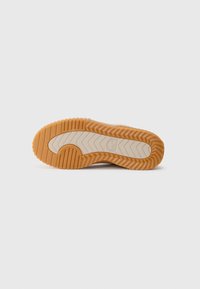 Såle av en tan og beige casual sko med en teksturert, rilleformet gummisåle og et sirkulært mønster nær hælen.