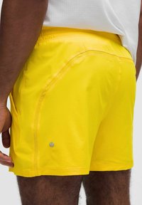 Klart gula träning short med en slät textur, elastisk midja och sidsömmar. Har logotypdetalj på nedre vänstra sidan.
