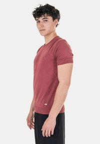 T-shirt rossa a maniche corte con scollo a V, realizzata in un tessuto morbido e con un design aderente. Presenta polsini ribattuti e un piccolo etichetta del brand all'orlo.