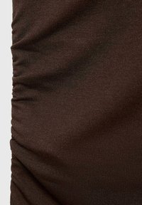 Tessuto elastico marrone con una superficie liscia e dettagli arricciati. Il primo piano mostra il motivo a maglia uniforme e la morbida caduta del materiale.