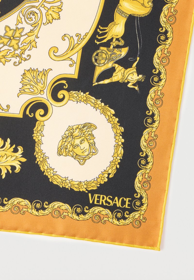 Silk scarf corner with gold baroque patterns, Medusa head emblem, chariot figure on black, cream, and orange background, "Versace" lettering.