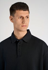 Czarna koszulka polo z klasycznym kołnierzykiem, z trzema guzikami z przodu i krótkimi rękawami. Wykonana z miękkiego, gładkiego materiału o subtelnej teksturze.