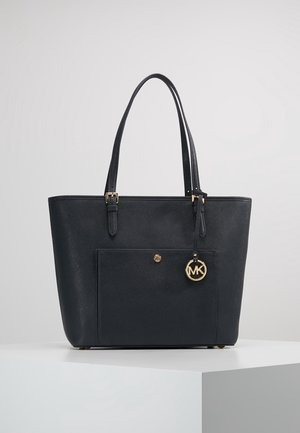 Sac cabas en cuir noir avec doubles bretelles, poche avant et breloque dorée circulaire avec logo MK suspendue à une bretelle.