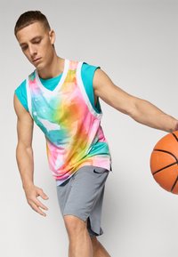 Fargerik basketball-drakt med et gradient akvarellmønster i rosa, grønt og blått, sammen med grå shorts og en basketball.