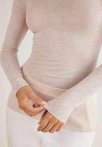 Ljusrosa långärmad topp gjord av tunt, mjukt tyg. Fitted design med en subtil textur och utställda ärmslut. Skräddarsydd för att följa kroppens konturer.