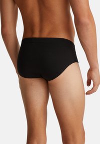 Slip in cotone nero con una texture liscia, design a vita bassa e cintura elastica, caratterizzato da una vestibilità attillata e cuciture pulite.