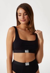 Svart ribbad crop-top med breda axelremmar och märkeselastiskt band; matchas med hög midja svart ribbat underkläder med matchande branding.
