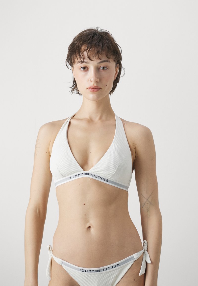 Hvit bikini-sett med trekantet haltertop med teksturert overflate og en bånd prydet med et logo; matchende bunn med sideknuter.