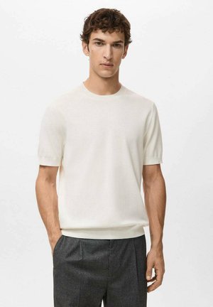 Suéter blanco de manga corta con cuello redondo, confeccionado con tela suave, que presenta una textura lisa y un diseño minimalista. Combinado con pantalones oscuros.