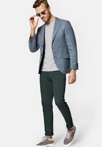 Niebieska marynarka w kratę, szary t-shirt, ciemnozielone spodnie i szare trampki; okulary przeciwsłoneczne; elegancki fason o dopasowanym kroju i fakturowanej tkaninie.