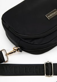 Černá nylonová taška přes rameno se hladkým povrchem, zlatými kovovými prvky, zipovým uzávěrem a tkaným popruhem se jménem značky.