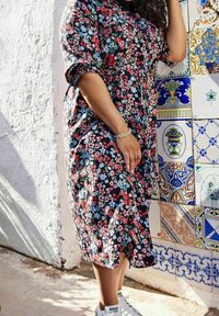 Blumenkleid mit schwarzem Hintergrund und roten, rosa sowie blauen Blumen, kurzen Puffärmeln und tailliertem Schnitt, kombiniert mit weißen Turnschuhen.