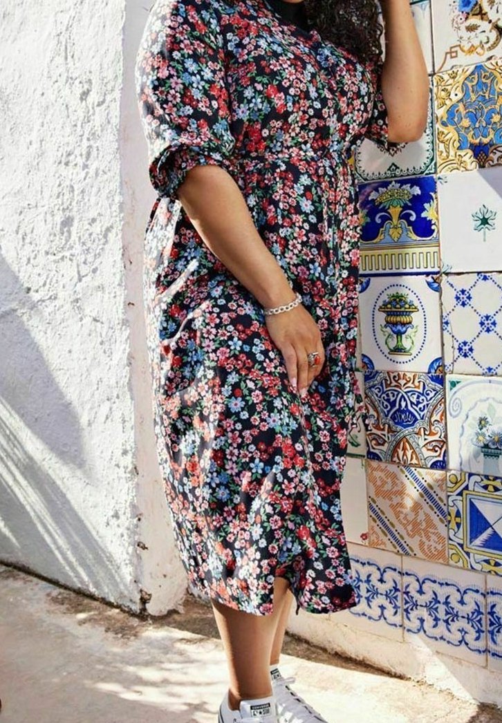 Blumenkleid mit schwarzem Hintergrund und roten, rosa sowie blauen Blumen, kurzen Puffärmeln und tailliertem Schnitt, kombiniert mit weißen Turnschuhen.