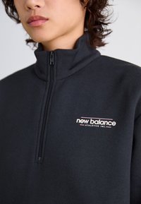 Sweat-shirt noir zippé avec un col montant, une texture douce et un logo subtil en rose et blanc sur la poitrine.