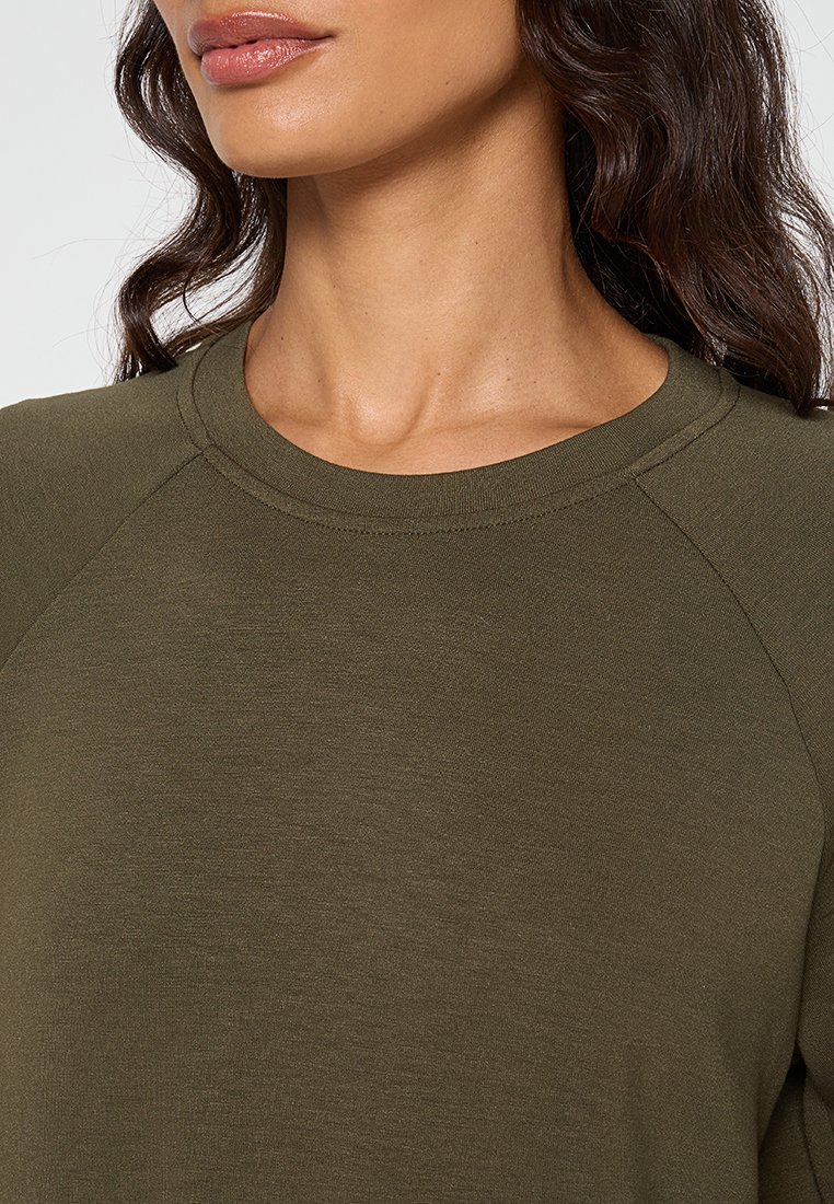 Felpa verde oliva con scollo rotondo, caratterizzata da una texture liscia e maniche raglan, che mette in evidenza un design semplice e minimalista.