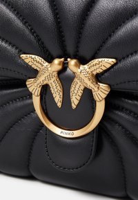 Zwarte, gewatteerde leren tas met een gouden ringklem met twee vogelaccenten en een geperst logo. Soepele textuur met gedetailleerde stiksels.