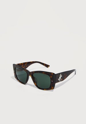 Lunettes de soleil œil de chat écaille de tortue avec verres verts foncés et logo "J" argenté sur les branches, présentées sur un fond blanc.