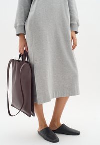 Graues langärmliges Kleid aus weichem Stoff, eine dunkelbraune Lederhandtasche mit Griffen und schwarze Rutschschuhe aus glattem Material.