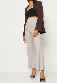 Hnědý blejzr, černý přiléhavý crop top, světle šedé žebrované zvonové kalhoty a černé vysoké podpatky. Hladké textury, ležérní střih.